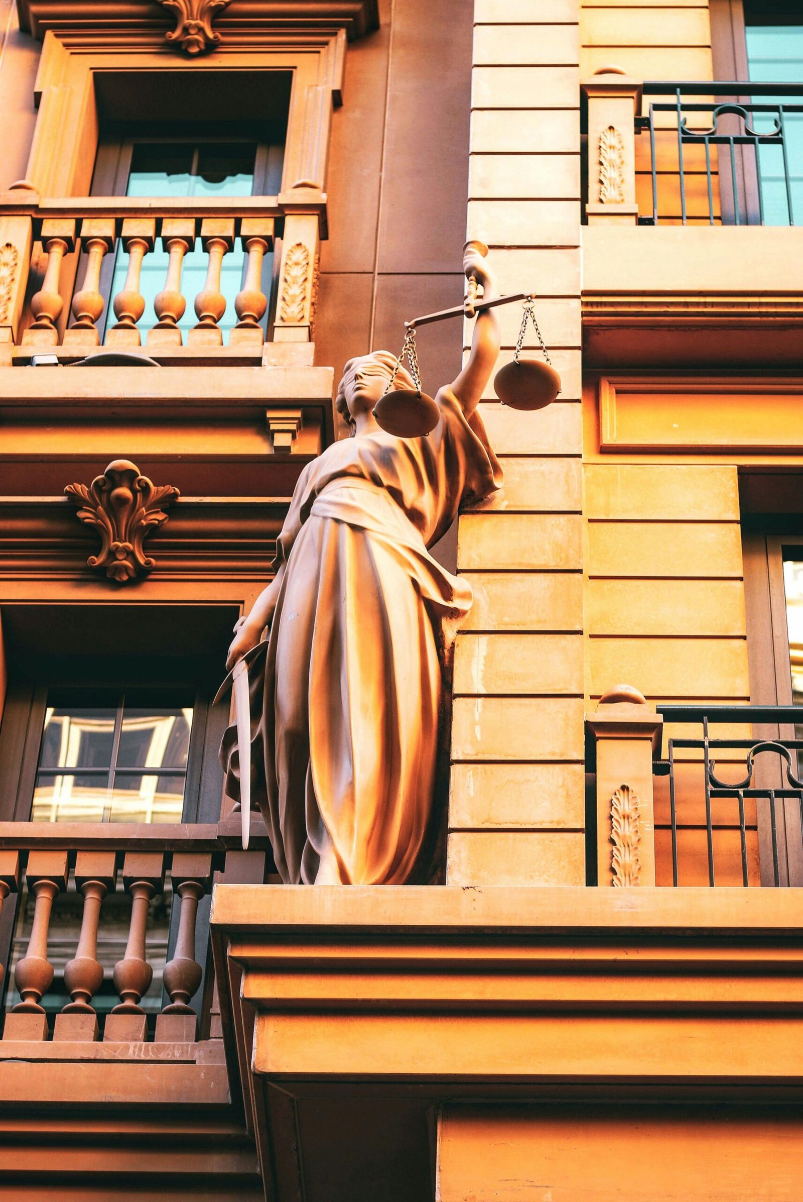 Statue of Lady Justice holding scales on a building facade, symbolizing law and fairness.