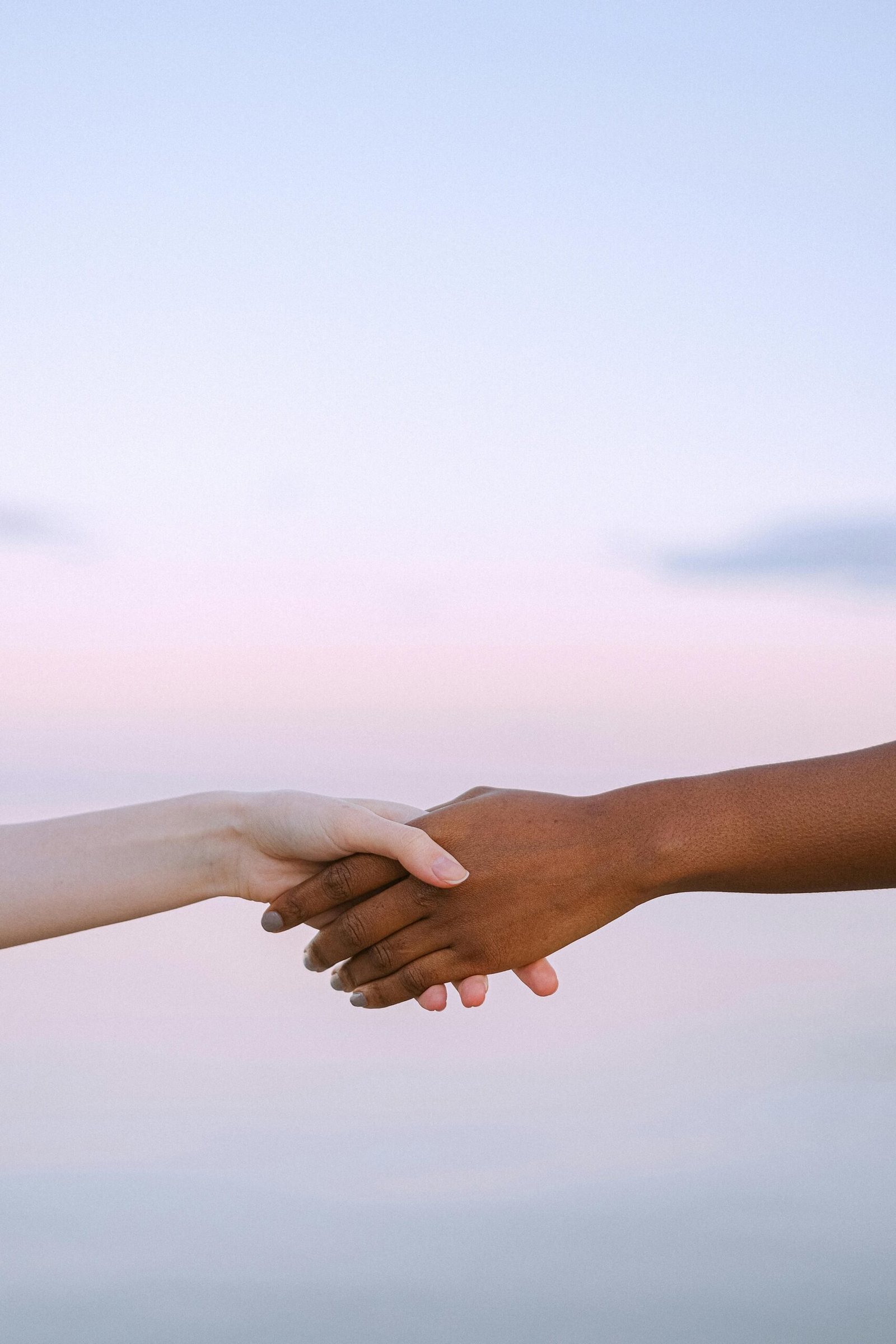 Two hands of different skin tones clasped together in unity and support.