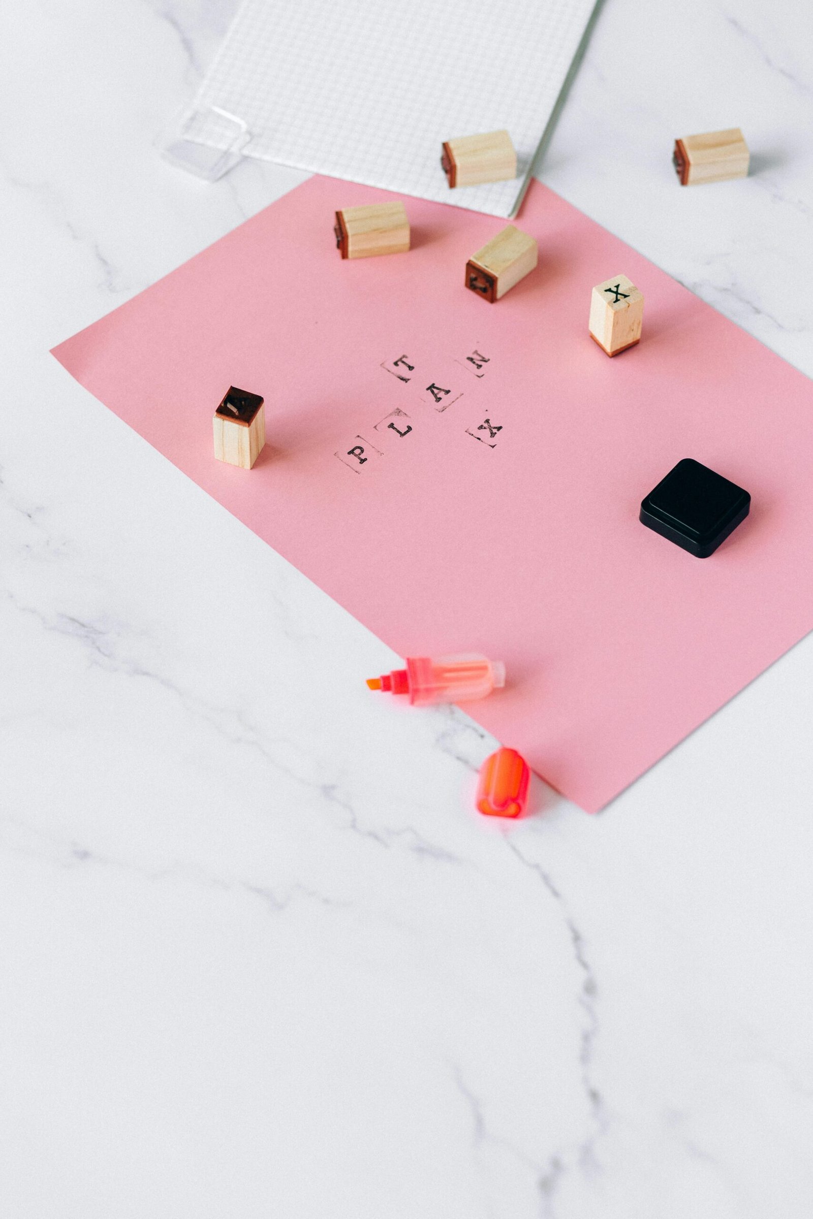 A flat lay of pink paper with planning stamps on a marble surface, symbolizing creativity and organization.