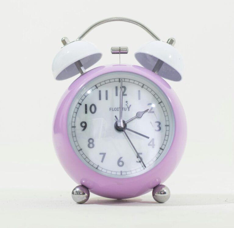 Lilac retro alarm clock with white face and bells on a plain background.